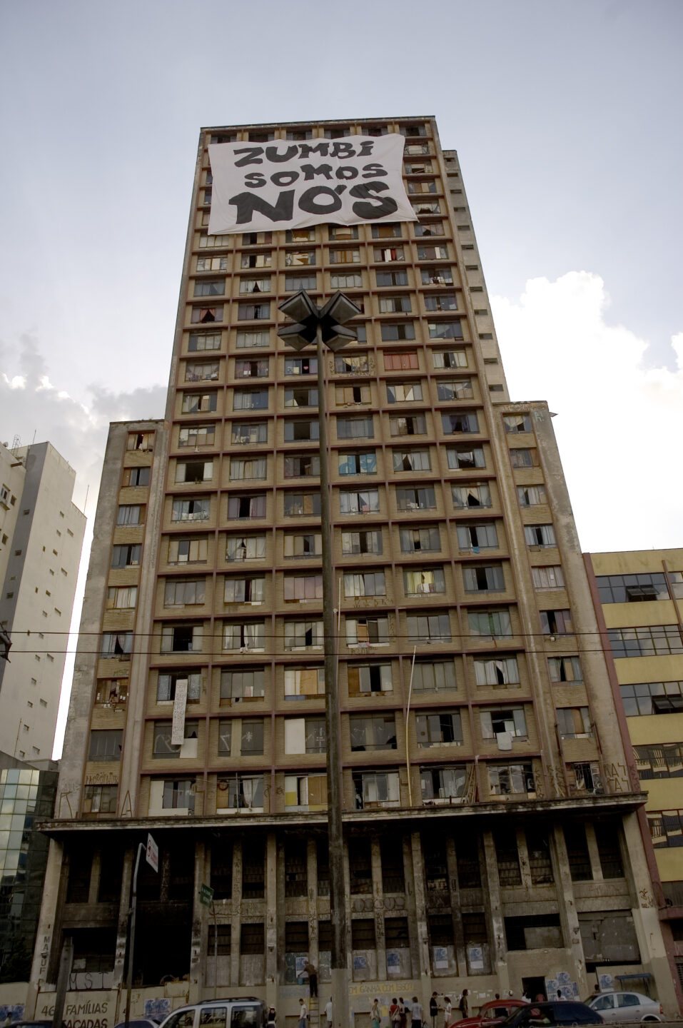 Foto de um prédio onde existe a Ocupação Prestes Maia com faixa da Frente 3 de fevereira presa no teto que diz "Zumbi somos nós".