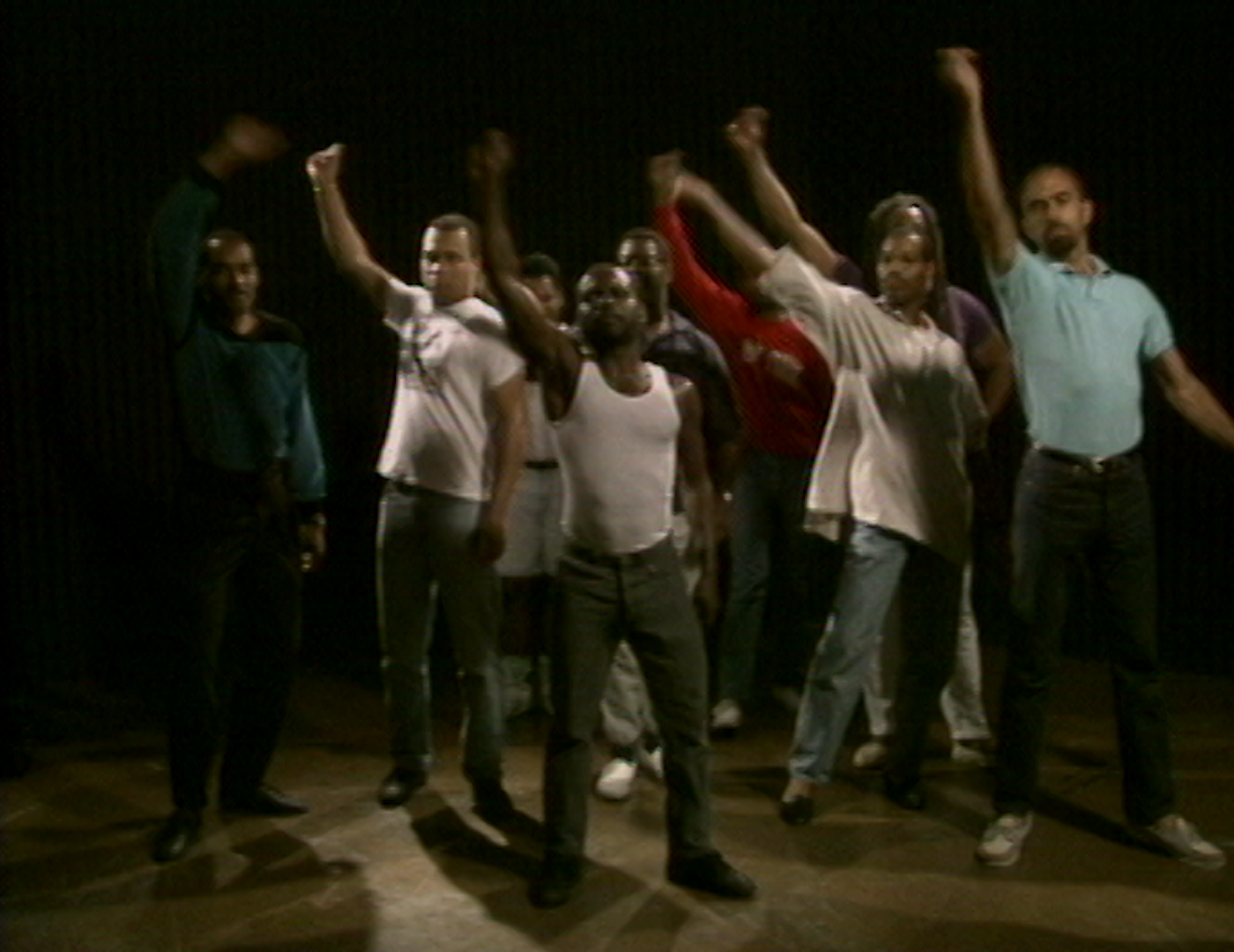 Foto de um grupo de pessoas em pé, com um homem negro ao centro, todos com a mão direita levantada e punhos cerrados.